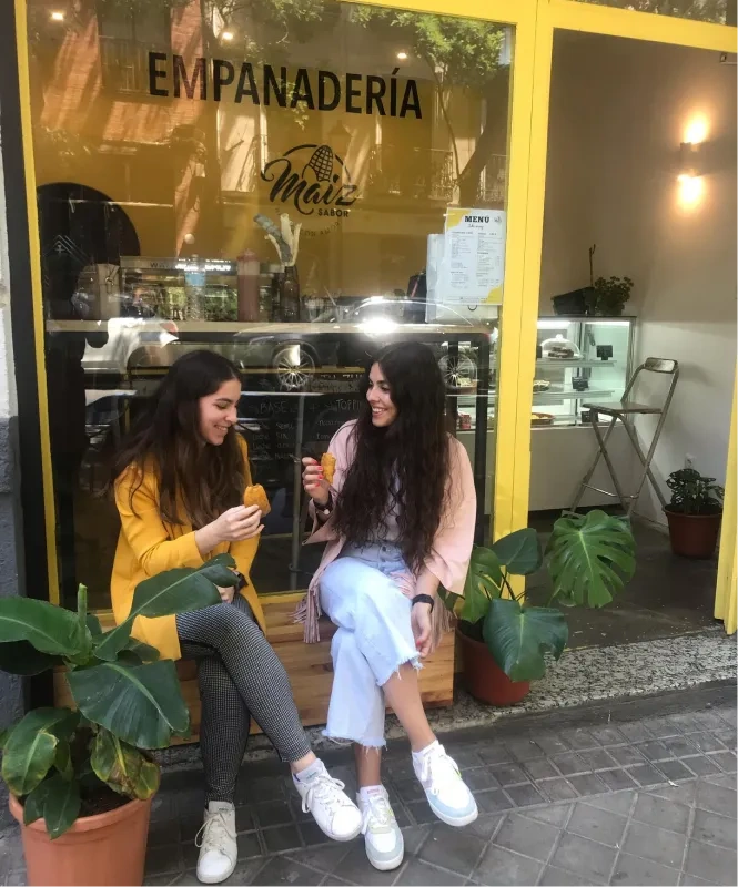 Dos mujeres disfrutando de las mejores empanadas colombianas de Madrid frente a empanadería Maíz Sabor